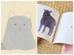 緑色の目をした灰色の猫のイラストと、角のある黒い動物のイラストが描かれた開かれた本が並べられた画像です。本は織物のマットの上で持たれています。