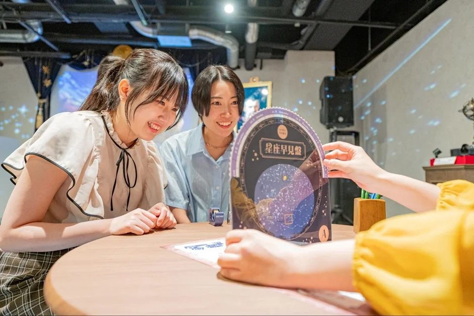 二人の若い女性がテーブルで笑顔で星座早見盤を覗き込んでいる