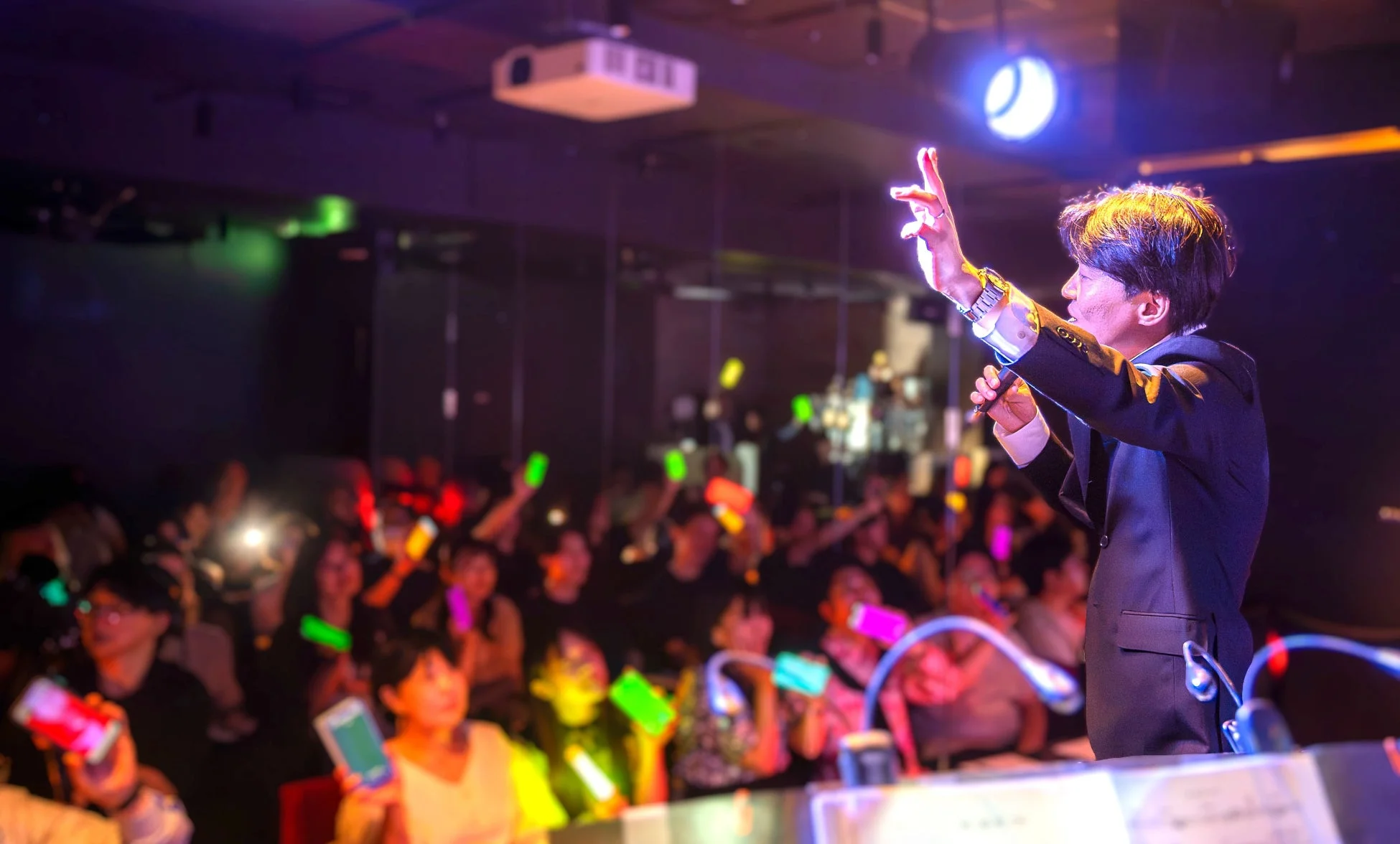 ライブイベントの様子、ステージ上の男性と光るスマートフォンを掲げる観客