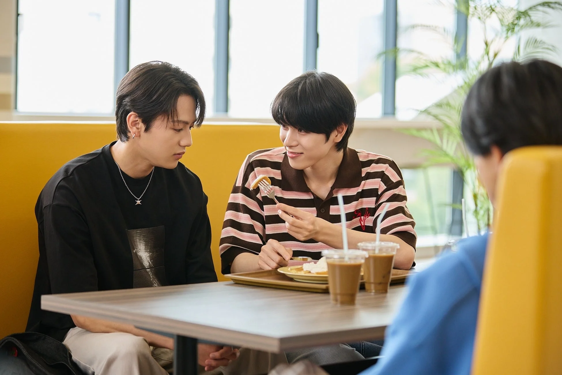 カフェのような場所で、2人の若い男性がテーブルを囲んで食事をしています。