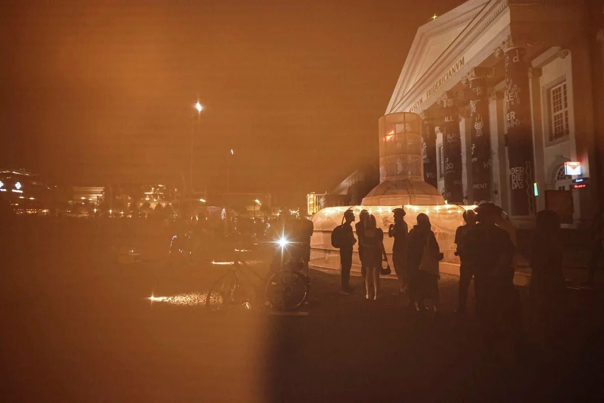 オレンジ色の光に包まれた夜の博物館「MUSEUM FRIDERICIANUM」前のアートインスタレーションと人々